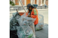 Image A man collecting trash on the street while holding trash bags.